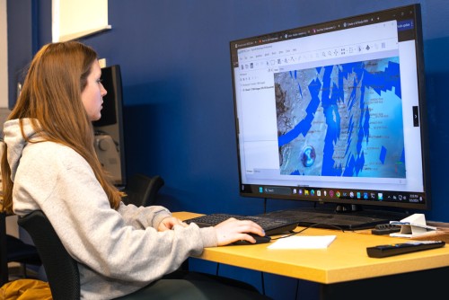 A Marine Science student looks at visualized data of coral reef maps on a large monitor