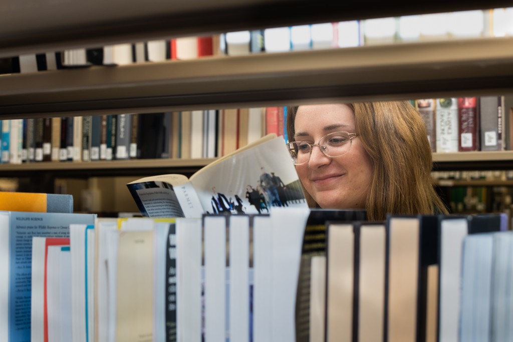 A U N E students read a book behind a bookshelf