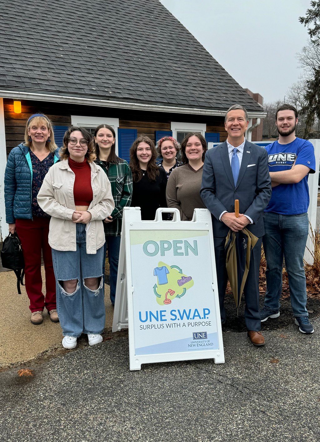 President Herbert stands with U N E students behind an "Open" sign for the Swap Shop