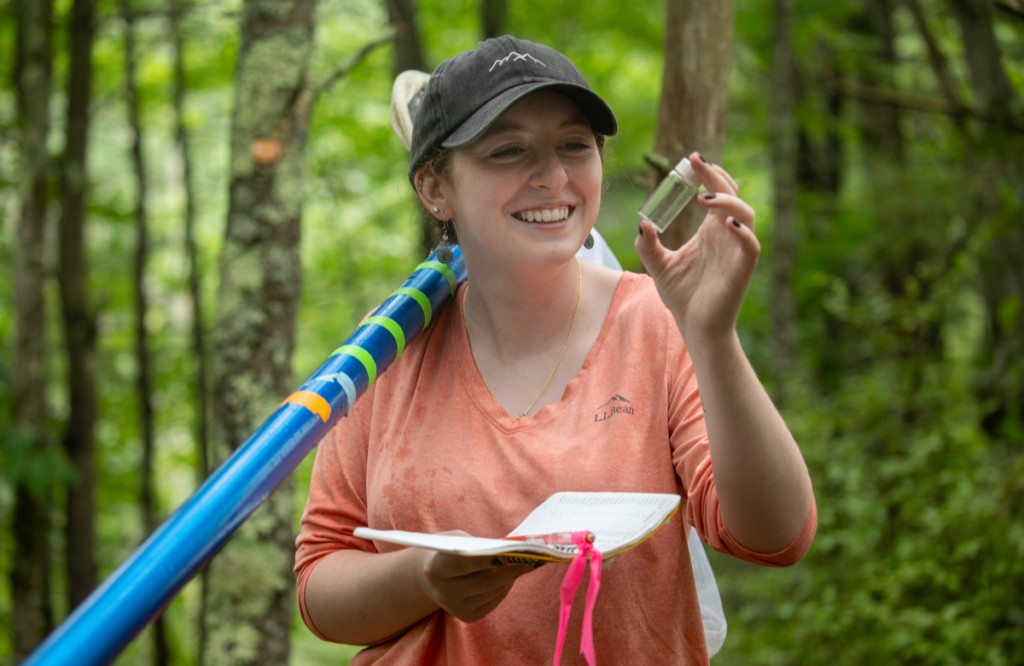 A student holds up a vial while doing research in a forest