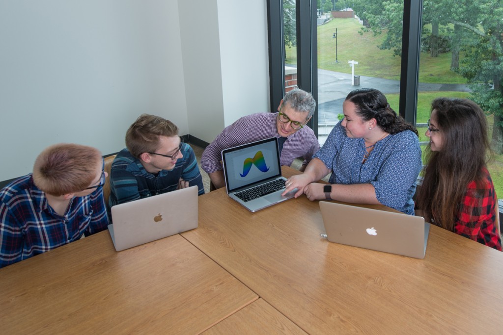 A professor reviews a student's graph in a classroom with three other students