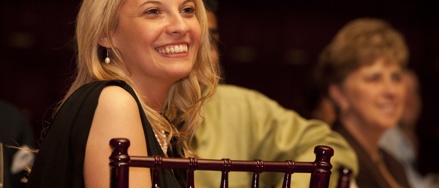 A female U N E pharmacy student sits smiling at a black tie event  