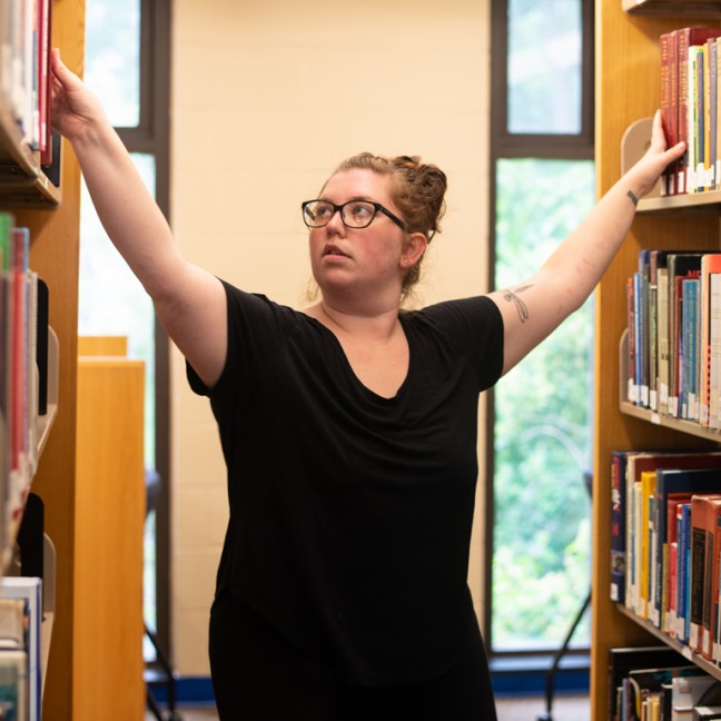 a student reaches for books on shelves on either side of her