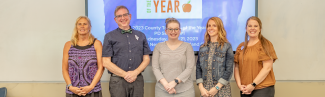 Five UNE alumni — Dawn McLaughlin, Joshua Chard, Lacey Todd, Katie Flannery, and Emily Rosser — are pictured against a whiteboard