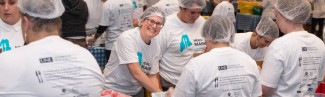 A volunteer smiles through the crowd of others helping to pack meal kits for the Meals for Maine event