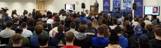 A crowd of students listen to a speaker at a podium